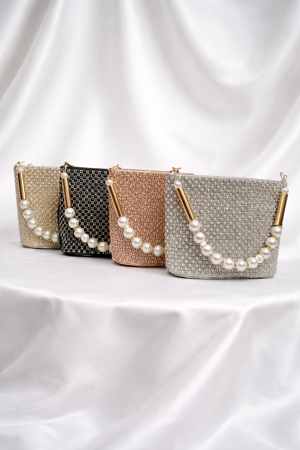 Four handbags with pearl embellishments on a white fabric background