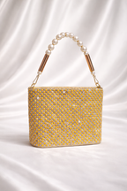 Yellow beaded handbag with pearl handle on a white satin background