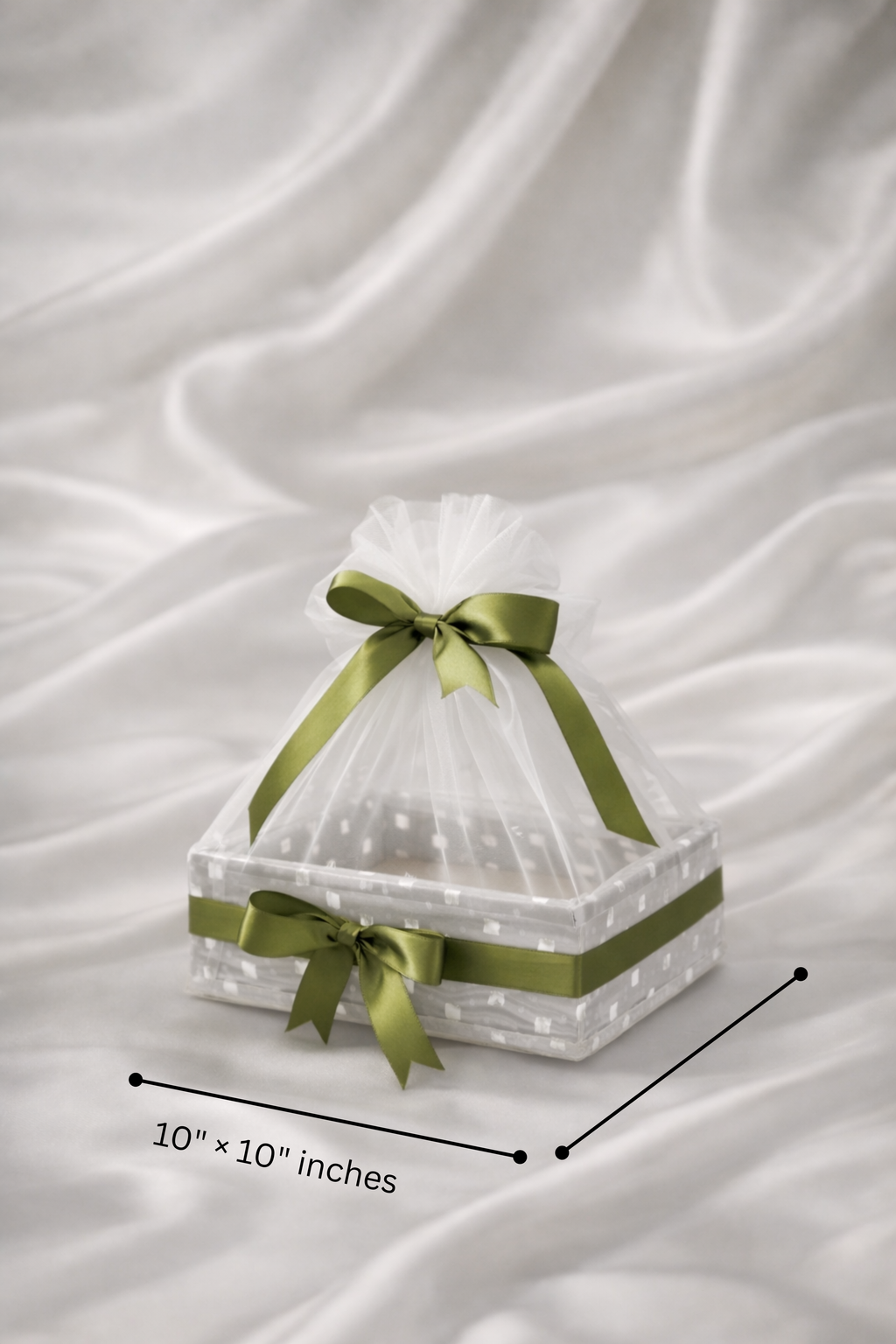 Clear cake stand with green ribbons on a white fabric background