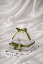 Clear cake stand with green ribbons on a white fabric background