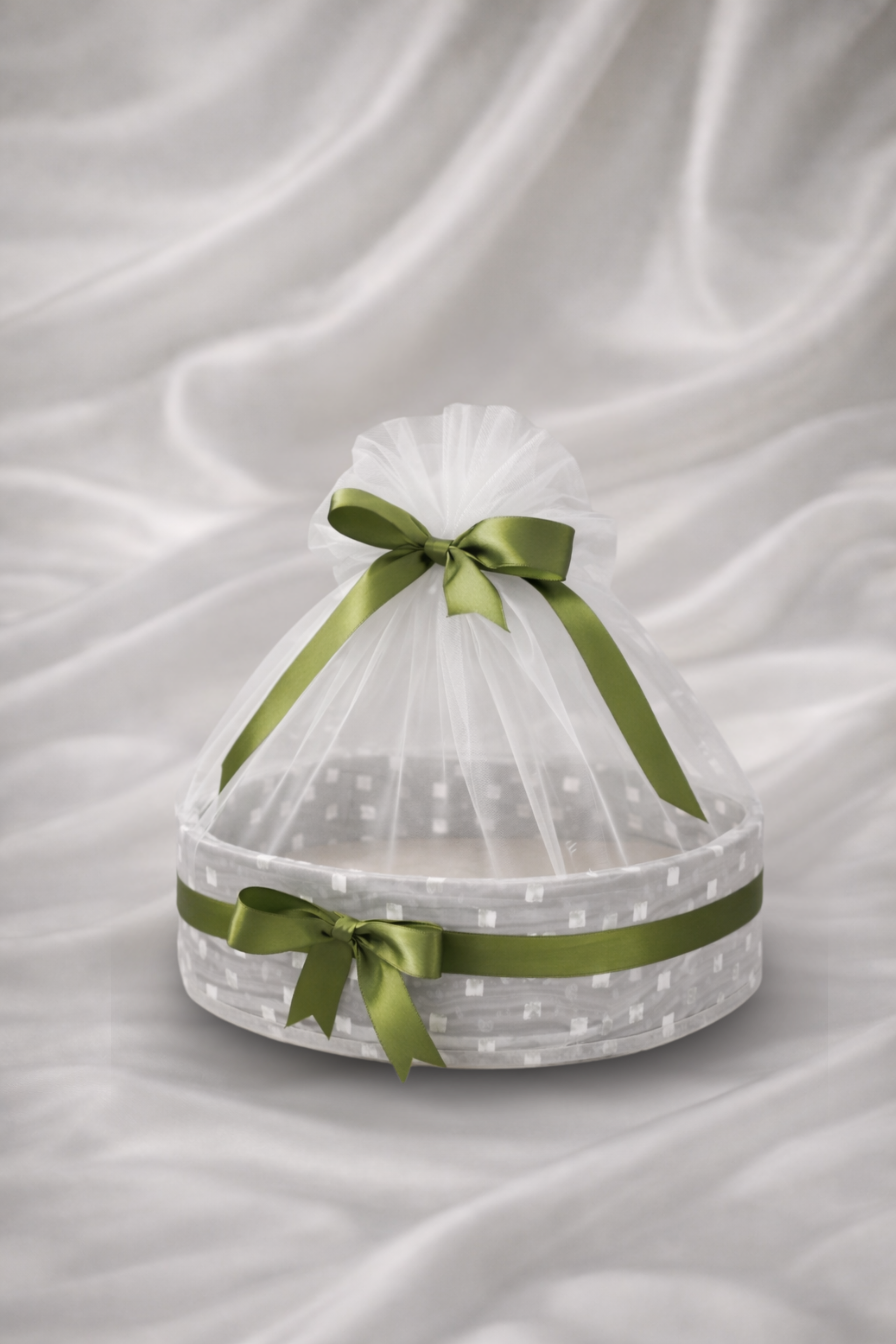 Decorative crystal basket with green ribbons on a white fabric background