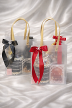 Two clear gift bags with black and red ribbons on a white fabric background
