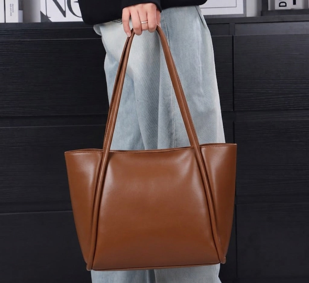 Person holding a brown leather tote bag against a black background