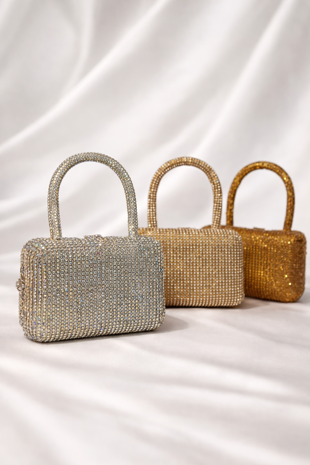 Three beaded handbags in silver, gold, and bronze on a white fabric background