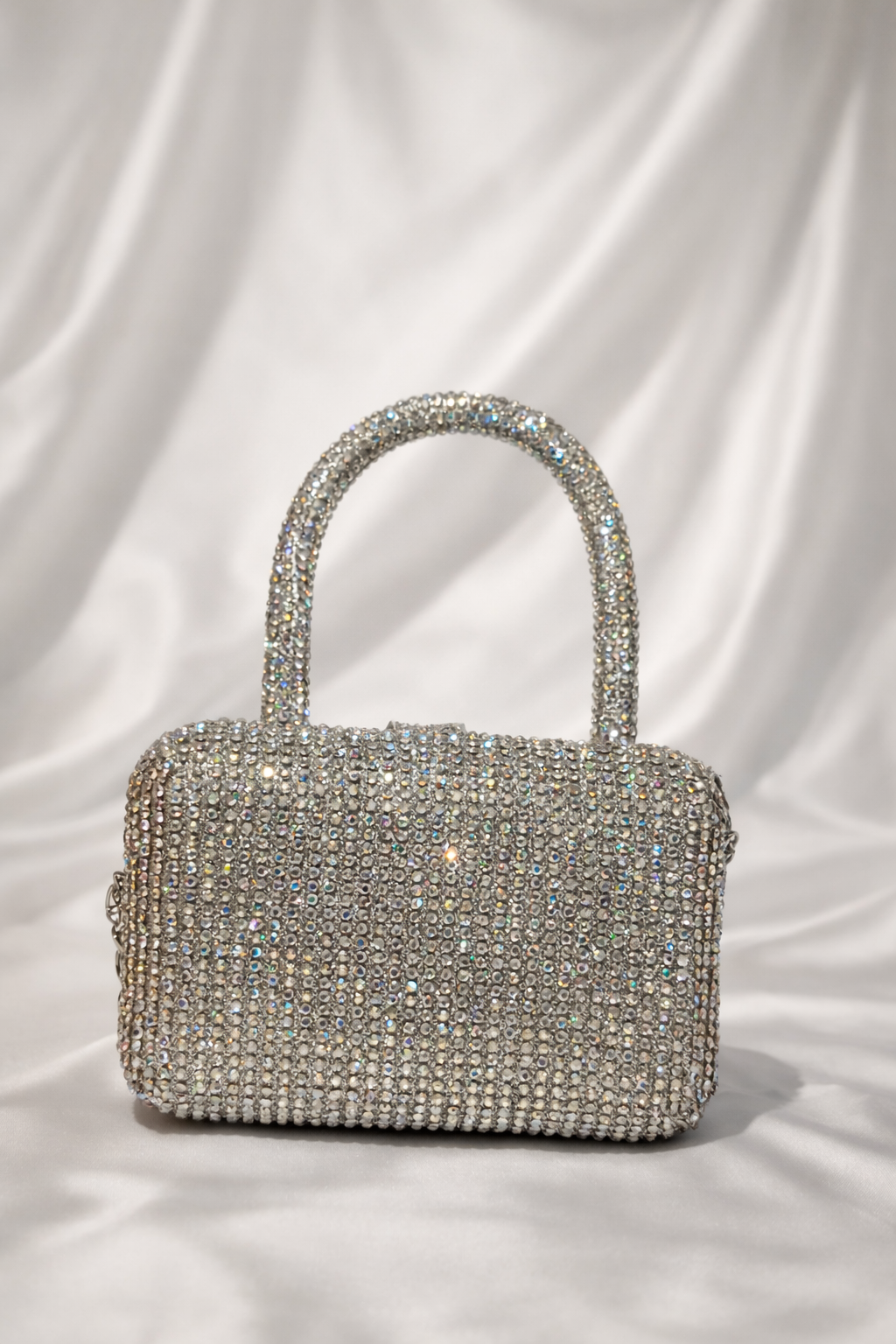 Silver handbag with rhinestone embellishments on a white fabric background